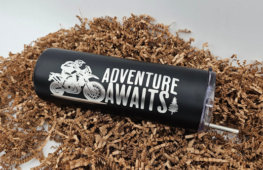 Front view of laser-engraved tumbler with motorcycle design and 'Adventure Awaits' inscription, lying on its side.