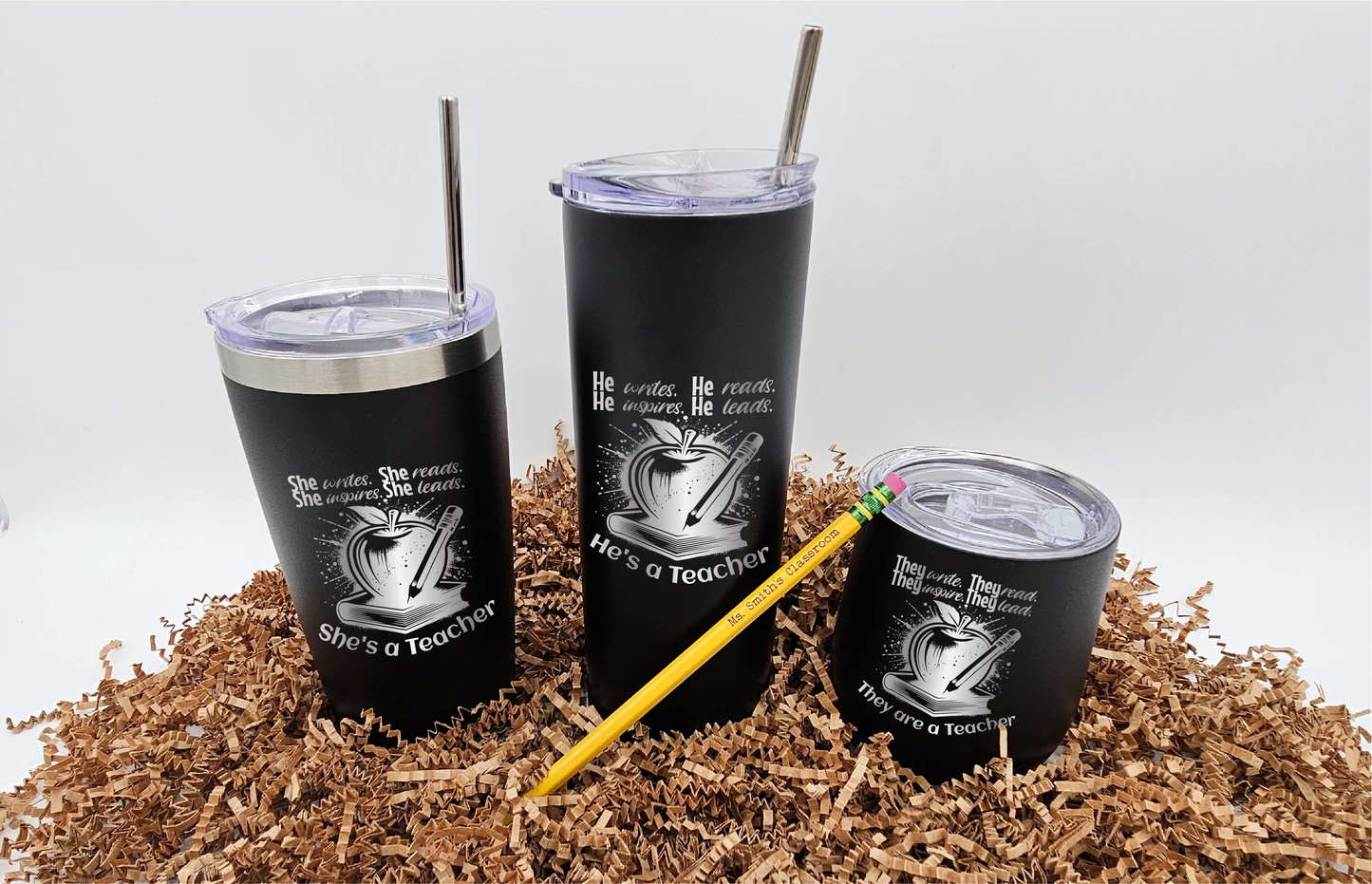 Three sizes of tumblers, each laser engraved with symbols representing teaching: a book, apple, and pencil, featuring different pronouns: they write, they read, they inspire, they lead; they are teachers. A laser-engraved pencil in front reads 'Ms. Smith's Classroom'. Displayed against a white backdrop.