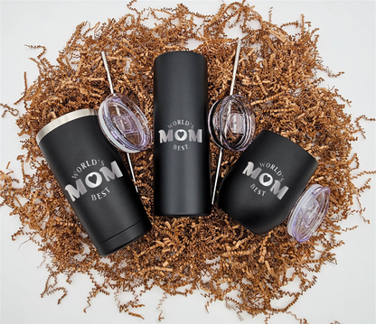 Three stainless steel tumblers of varying sizes, each engraved with 'World's Best Mom' horizontally, resting on crinkled brown paper.