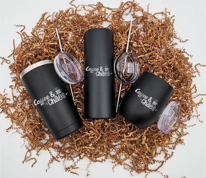 Three stainless steel tumblers of varying sizes, each engraved with 'Coffee & Chaos' horizontally, resting on crinkled brown paper.