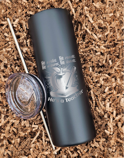 Front-facing view of a sleek 20 oz. skinny tumbler against a textured brown crinkled paper backdrop. The tumbler is laser engraved with detailed images of a book, apple, and pencil, accompanied by the text 'He writes, he reads, he inspires, he leads; he's a teacher.' The engraving captures the essence of education and dedication, making it the perfect gift for any passionate educator.